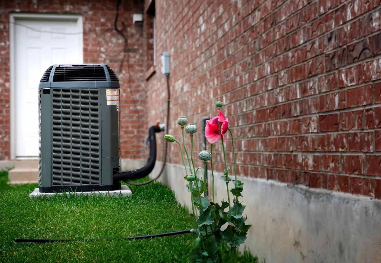 Central air conditioner condenser beside a brick home