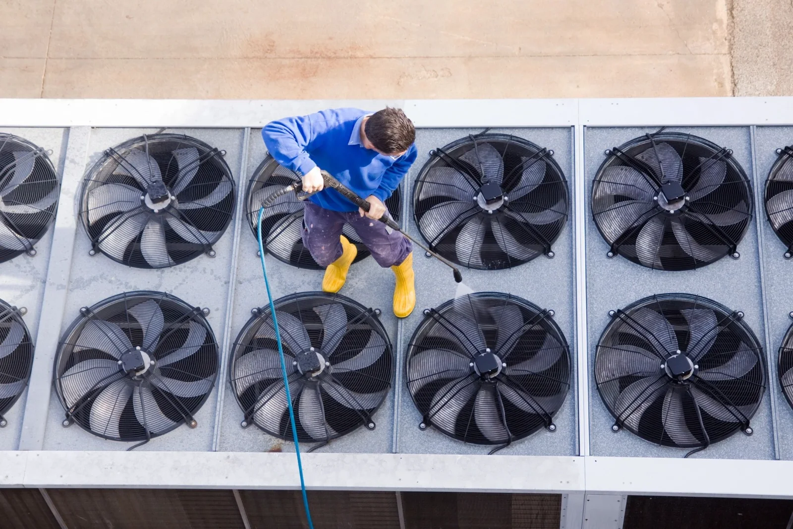 Technician cleaning rooftop condenser fans on a commercial building