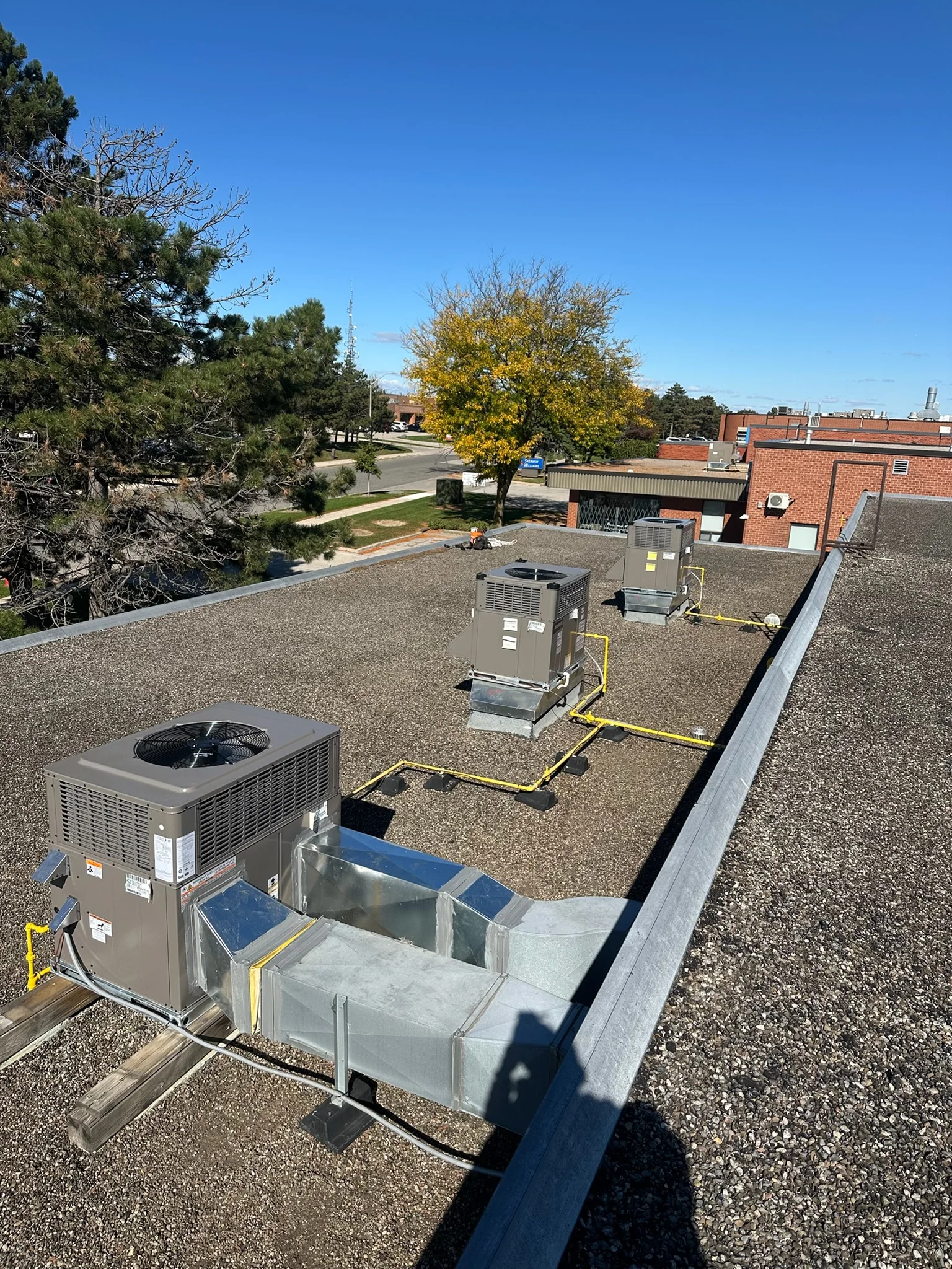 Three new packaged rooftop units with gas piping on a commercial roof